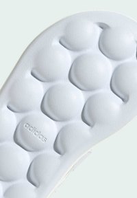 Suela de zapato de goma blanca con una superficie texturizada que presenta patrones de burbujas redondeadas. Logo "adidas" grabado cerca de la parte inferior.