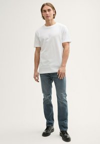 Fehér pamut póló, rövid ujjú, világoskék farmernadrággal párosítva. Fekete bőrcipő egészíti ki az öltözetet. Egyszerű dizájn, minta nélkül.