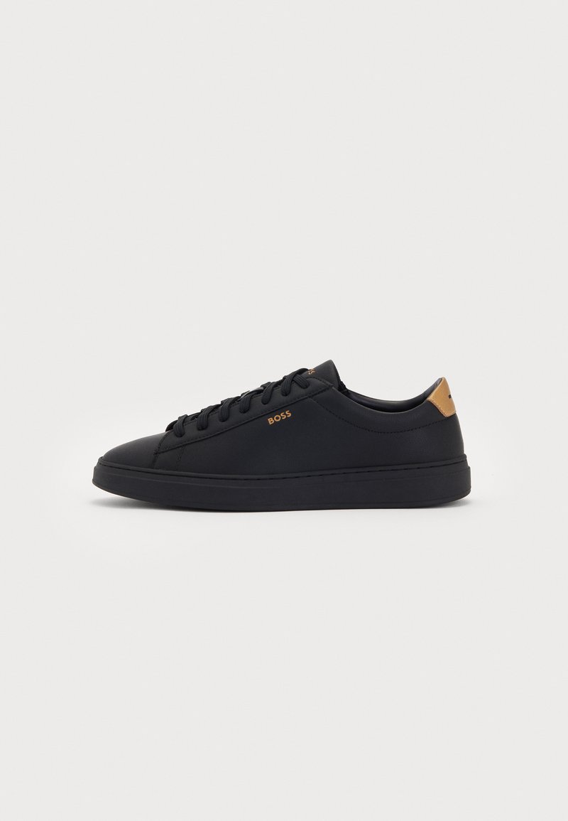Sorte lav-sneakers med snøring foran, tan hælflap og "BOSS" logo på siden, vist på en hvit bakgrunn.