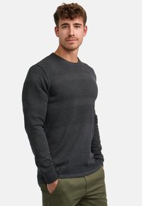 Dunkelgrauer gestrickter Pullover mit strukturierten horizontalen Streifen. Rippbündchen und Saum; taillierte Silhouette. Kombiniert mit olivgrünen Hosen.