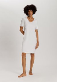 Camicia da notte bianca a maniche corte con scollatura a V, rifinitura in pizzo sulle maniche e taglio dritto, realizzata in tessuto morbido. Modella sta in piedi a piedi nudi.