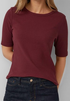 Bordowa prążkowana koszulka z krótkimi rękawami, okrągłym dekoltem i dopasowanym krojem, zestawiona z ciemnymi jeansami z przodu zapinanymi na guziki.