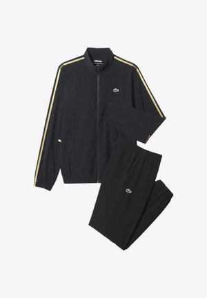 Survêtement zippé noir avec des rayures dorées sur les manches et le pantalon, arborant un logo de crocodile vert sur la poitrine et la cuisse.