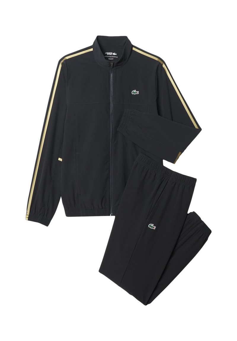 Schwarzer Zip-Up Trainingsanzug mit goldenen Streifen an Ärmeln und Hosen, mit einem grünen Krokodil-Logo auf der Brust und dem Oberschenkel.