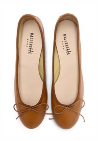 Ballerine in pelle marrone con punta arrotondata, bordo elastico e un piccolo fiocco davanti. Fodera interna di un leggero beige.