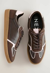 Brune sneakers med pinke detaljer og en gummisål, med snøreredesign og polstret krave, præsenteret på en lys baggrund.