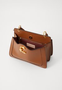 Brown leather handbag with gold hardware, a top flap, and a two-section interior featuring a zip pocket and brand label.