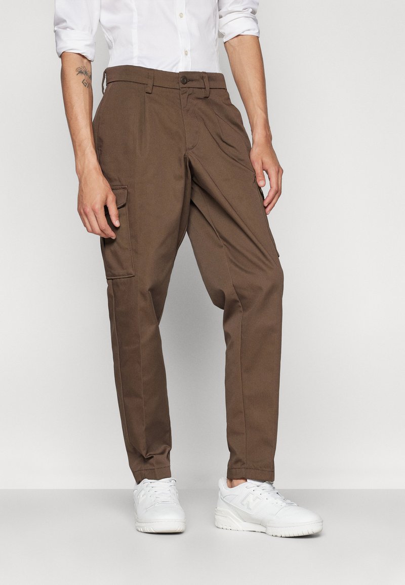 Brown cargo pants with a tailored fit, made of sturdy fabric. Features side pockets, a zip fly, and a button closure. Pair with white sneakers.