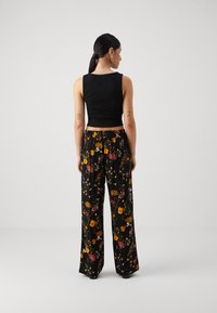 En sort cropped tank top kombinert med høytlivs vide bukser med blomstermotiv, der det fargerike blomstermønsteret står ut mot en svart bakgrunn.