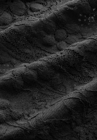 Schwarzer Stoff mit Struktur, der zarte Spitzenmuster aufweist, wobei unterschiedliche Dicken und gewebte Designs Kontraste und Tiefe erzeugen.