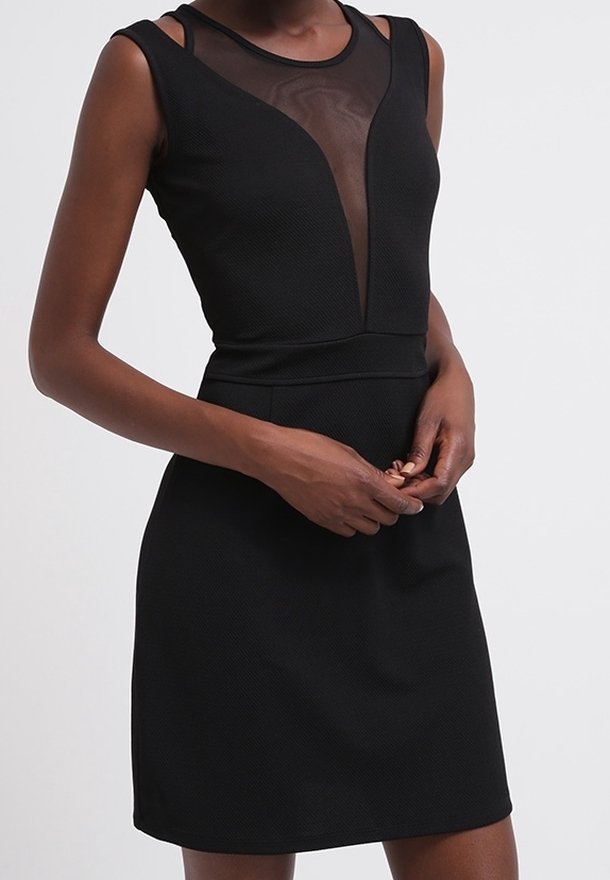 Robe noire sans manches avec panneau en maille transparente en V et tissu texturé, portée par une personne les mains légèrement croisées à la taille.