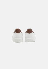 Weiße Sneakers mit braunen Lederakzenten an der Ferse, Gummisohle und strukturiertem Design, die einen minimalistischen Stil aufweisen und keine auffälligen Muster zeigen.