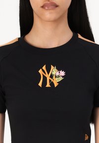 Juodas trumpas rankovėmis marškinėliai, kuriuose yra oranžinė siuvinėta "NY" logotipas su rožinėmis gėlėmis ir žaliomis lapai, apvaliu iškirpimu ir minkšta tekstūra.