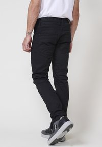 Črne jeans cargo hlače s ožjim krojem, z zadnjimi žepi in kontrastnimi šivi, v kombinaciji s sivimi supergami.