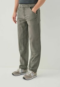 Green cotton pants with a relaxed fit, featuring front pockets and reinforced knee patches. Styled with gray sneakers.