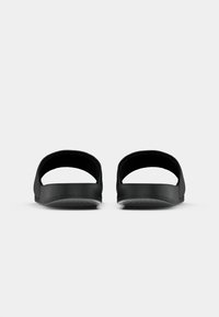 Sandales à glisser noires avec une arrière ouvert, une semelle plate et une texture lisse. Design minimaliste sans logos ni motifs visibles.