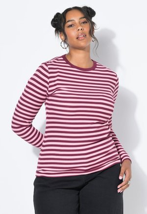 T-shirt ajusté à manches longues, orné de rayures horizontales en rouge foncé et rose clair. Encolure ronde et texture côtelée. Pantalons noirs portés en dessous.