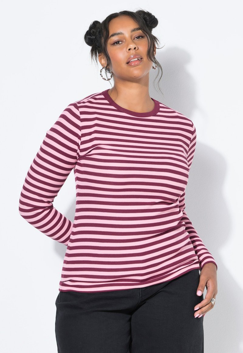 T-shirt ajusté à manches longues, orné de rayures horizontales en rouge foncé et rose clair. Encolure ronde et texture côtelée. Pantalons noirs portés en dessous.