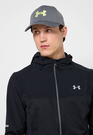 Jeune homme regardant vers la droite, portant une casquette grise avec un logo néon et un sweat à capuche zippé noir avec un logo de marque réfléchissant sur la poitrine.