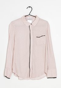Camisa de manga larga con botones en tela rosa claro con lunares negros, detalles en negro, un cuello y un bolsillo único en el lado izquierdo.