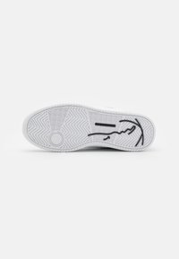Fehér sneaker talp, textúrált tapadó mintázattal, kör alakú logóval és fekete stilizált grafikával. Simító gumi anyag.