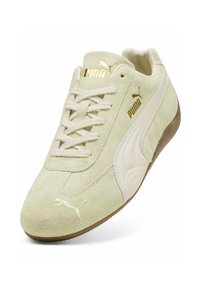 Zapatilla de ante verde claro con una superficie texturizada, acentos en crema, logo dorado y cordones. Presenta una suela de goma y un diseño atlético clásico.