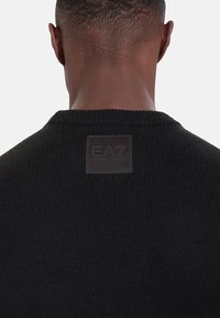 Maglione nero lavorato a maglia con scollo rotondo, tessuto testurizzato e etichetta quadrata del marchio EA7 sul retro.