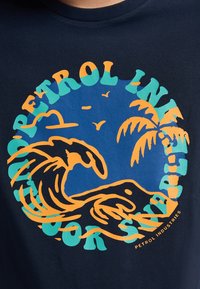 Marineblå T-shirt med et farverigt cirkulært grafisk design med en bølge, palmetræer og teksten "Petrol Industries" i orange og teal.