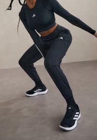 Zwart sportoutfit met een slim-fit lange mouwen top en taps toelopende broek. Opmerkelijke witte strepen op de broek en schoenen. Gelaagd stof.