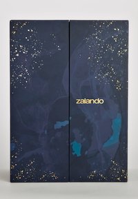 Niebieskie i ciemnoniebieskie pudełko z złotymi akcentami, z abstrakcyjnymi wzorami i wyraźnym złotym logo "zalando" na środku.