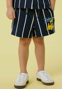 Shorts a righe navy con linee bianche, caratterizzati da una grafica di Pikachu giallo e una vita con cordino. Abbinati a sneakers bianche.