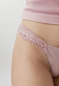 Κοντινό πλάνο ενός ατόμου που φοράει ροζ εσώρουχα με δαντέλα και ένα ταιριαστό ροζ τοπ, με έμφαση στην περιοχή των γοφών και της μέσης.