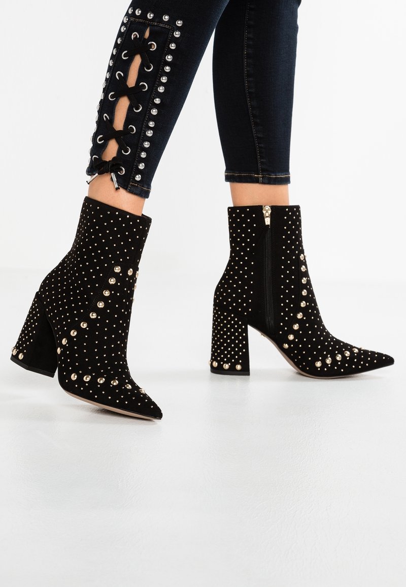 Musta mokkapohjaiset nilkkurit teräväkärkiset, koristeltu kultaisilla niiteillä, chunky-korko ja sivu vetoketju kiinnitystä varten.