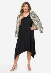 Schwarzes ärmelloses Kleid mit asymmetrischem Saum, darunter eine cremefarbene und schwarze Leo-Print-Jacke. Silbern strappy High Heels vervollständigen das Outfit.