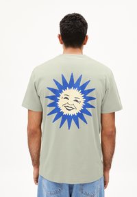 Groene katoenen t-shirt met een groot blauw zonontwerp met een lachend gezicht op de achterkant. Korte mouwen en een relaxed fit.