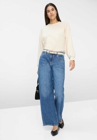 Camicia a maniche lunghe color crema, jeans a vita alta azzurri larga, cintura beige, borsa nera, ballerine nere, texture in denim liscio.