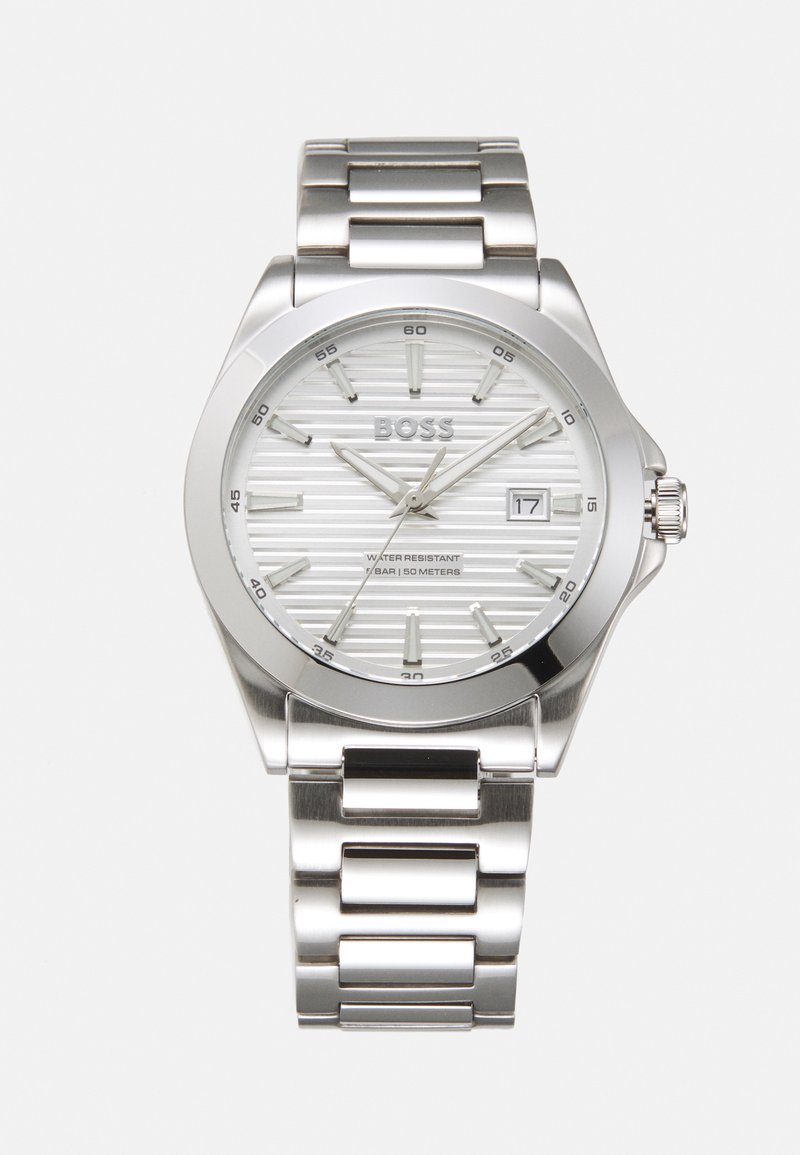 Reloj de acero inoxidable plateado con una esfera blanca texturizada, marcadores de horas plateados, display de fecha y una pulsera metálica de eslabones. Resistente al agua hasta 50 metros.