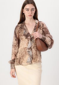 Langermet, mønstret bluse med v-hals og rynkedetaljer, i nyanser av brunt og beige, kombinert med en rund, brun veske.