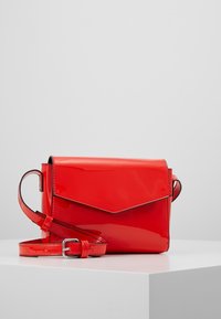 Bolso bandolera de charol rojo con cierre de solapa, correa ajustable y textura lisa y brillante. Diseño rectangular compacto.