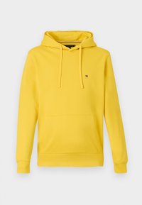 Žltá dlhá mikina s kapucňou, s prednou klokanou vreckou, sťahovacou kapucňou a malou vlajkou Tommy Hilfiger na ľavej hrudi.