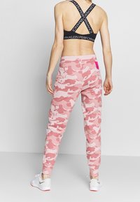 Różowe dresy w kamuflażu z dopasowanymi nogawkami i elastycznym pasem. Połączone z czarnym sportowym biustonoszem z krzyżującymi się na plecach ramiączkami i logo.