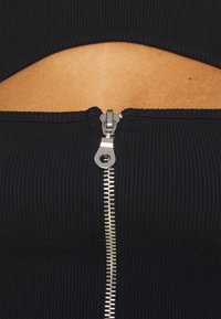 Top in tessuto nero a coste con chiusura con zip in metallo argentato sul retro, con un design a cut-out che espone la pelle. Texture liscia.