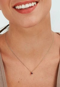Zartes goldfarbenes Halsband mit einer dünnen Kette, die einen kleinen, runden, lila Anhänger trägt. Das schlichte Design betont die Farbe des Anhängers.