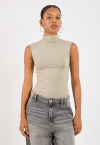 Haut sans manches beige à col roulé avec une coupe ajustée, associé à un jean en denim gris clair taille haute avec une finition décolorée.