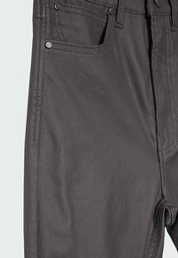 Gros plan sur un pantalon gris foncé montrant la poche avant, les détails de la couture et les rivets métalliques sur le tissu.