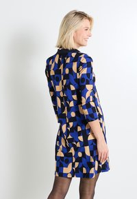 Vestido azul y negro con patrones geométricos, con mangas tres cuartos y escote redondo. Tejido texturizado.