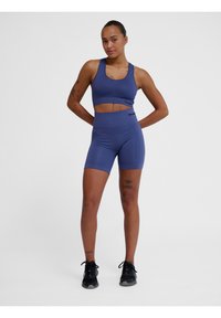 Lila sport-bh och högmidjade shorts gjorda av stretchigt material. Har en åtsittande design och svarta logodetaljer, tillsammans med svarta sneakers.