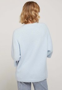 Un pullover oversize bleu clair en tissu doux, avec un col rond et des manches amples, associé à un pantalon à carreaux bleu et blanc.