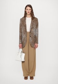 Blazer à imprimé léopard avec un bouton unique, associé à un pantalon taille haute beige, un haut blanc et un petit sac à main blanc. Chaussures marron.