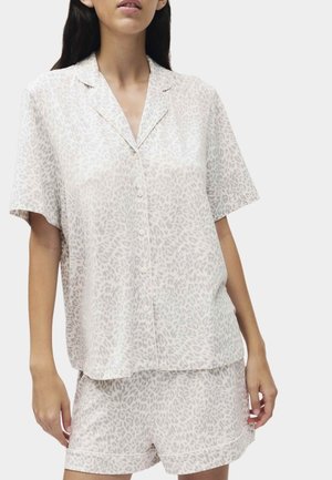 Frau trägt ein hellbeiges Kurzarmhemd mit Knöpfen und passende Shorts mit dezentem Leopardenmuster.